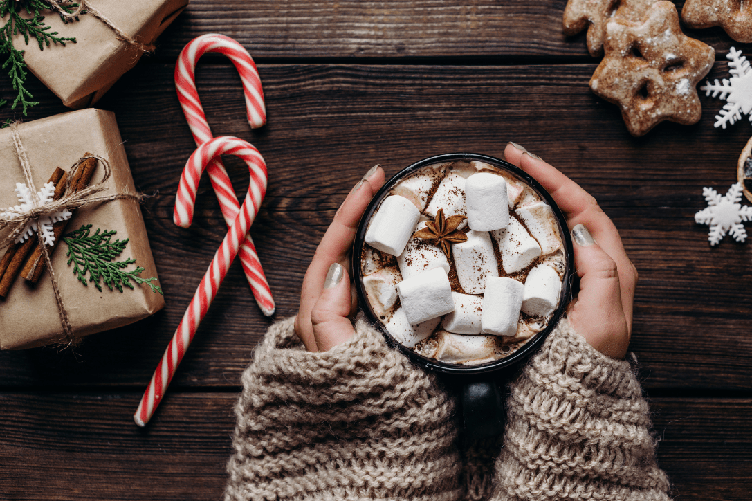 Personne se réchauffant les mains avec une tasse de chocolat chaud garnie de chamallows